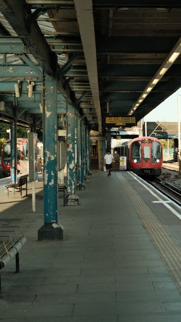 A modern passenger train with a sleek yellow and grey exterior travels along railway tracks beneath an old brick railway bridge, set in a green landscape with trees on either side. The train's surface