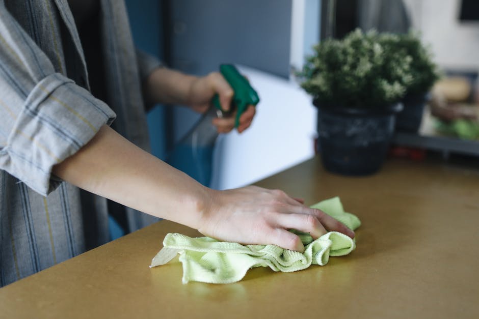 A flat lay of cleaning tools and supplies for surface cleaning and sanitisation, featuring bright pink rubber gloves, a green spray bottle with a blue trigger, a yellow and red sponge, a light pink spray bottle, and a pink cleaning cloth. The items are arranged on a white surface, indicating a setup for domestic or commercial cleaning, with a focus on hygiene and maintenance. This image aligns with Putney Cleaners' expertise in detailed and professional cleaning services in residential flats along Upper Richmond Road, as highlighted in the context of the page 'Cleaning Upper Richmond Road Flats: Local Tips, PUTNEY' available at putney-cleaners.org.uk, ensuring a clear visual representation of cleaning processes.
